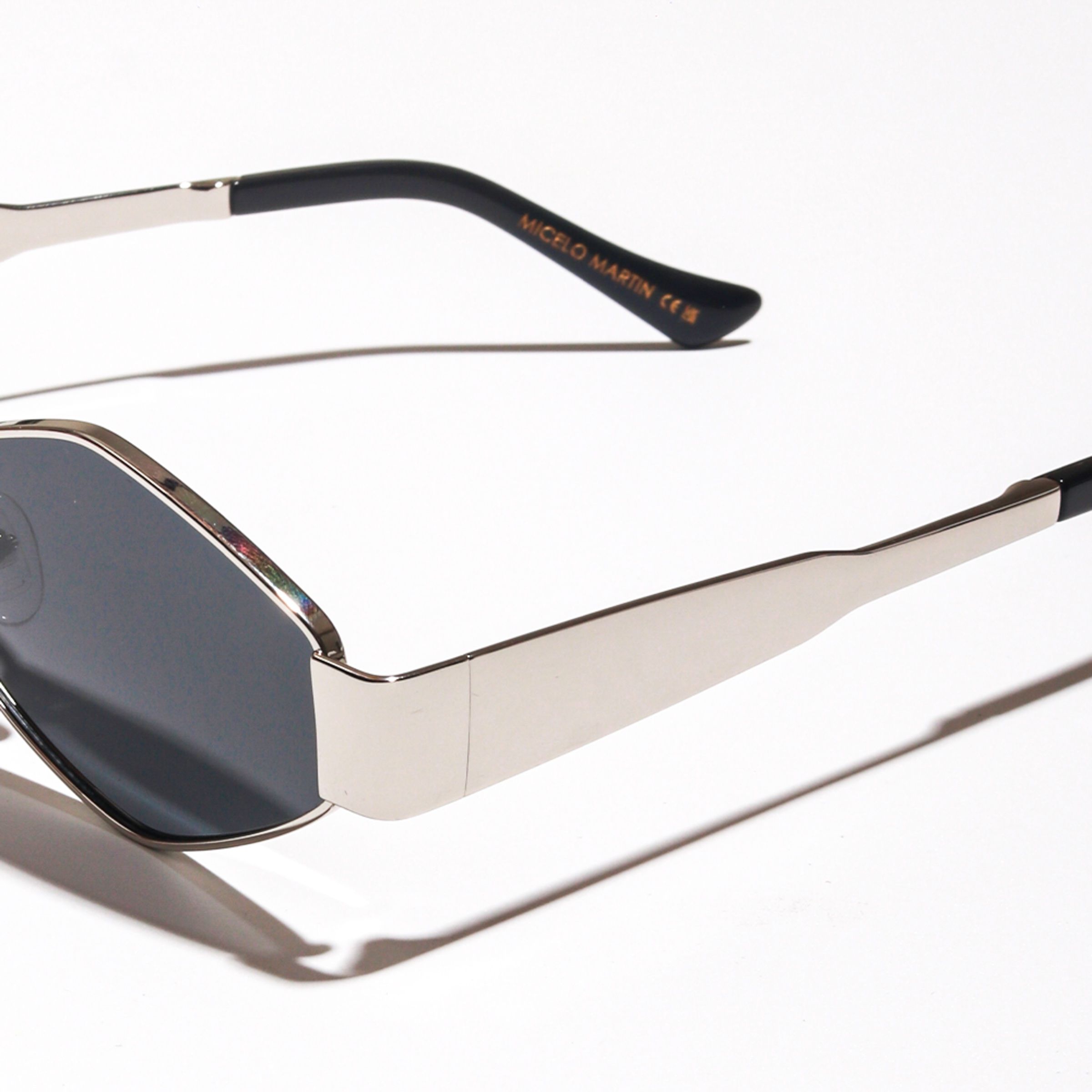 Micelo Martin sunglasses with a silver metal frame and dark lenses, the label’s name printed on the temple tip.